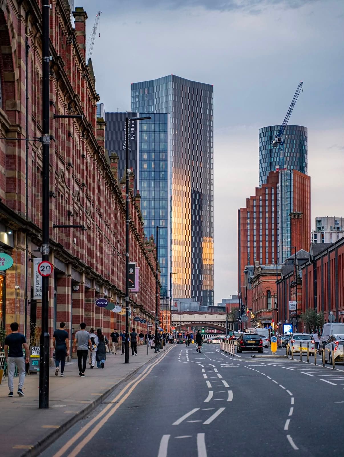 Deansgate looking toward the Deansgate Square towers at dusk, red-brick warehouses lining the Manchester street